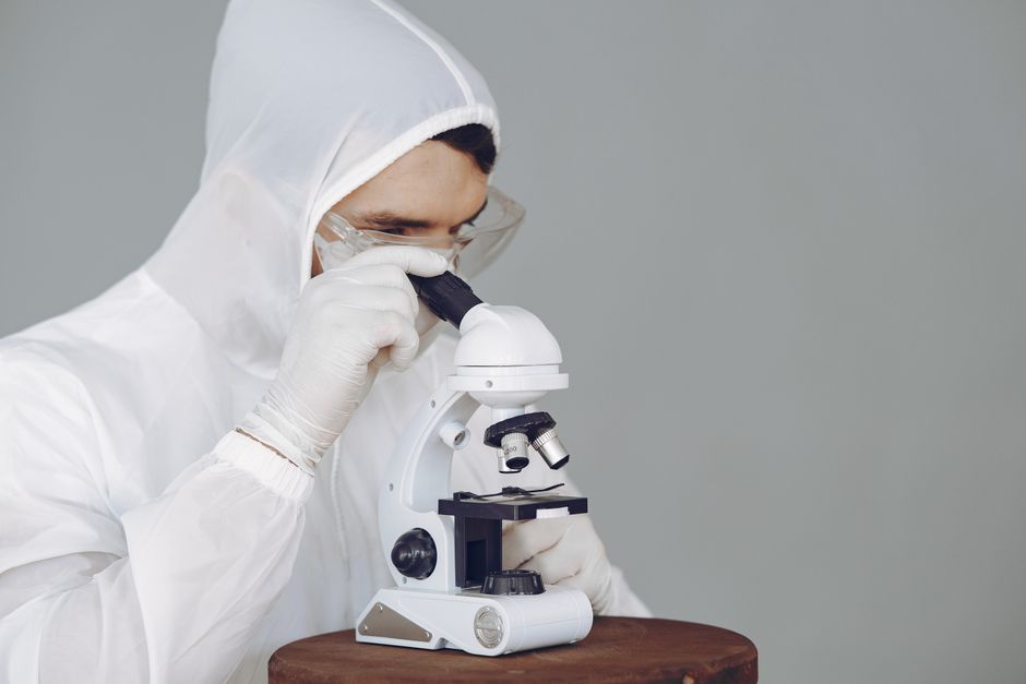 Scientist in protective gear using a microscope, focused on research and analysis.