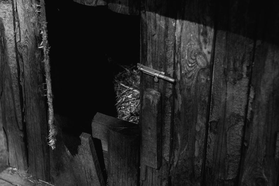 Black and white photo of an old wooden henhouse with hay inside.